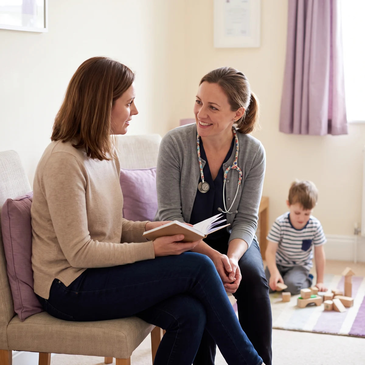 A mom talking with a doctor while her son plays with blocks nearby
