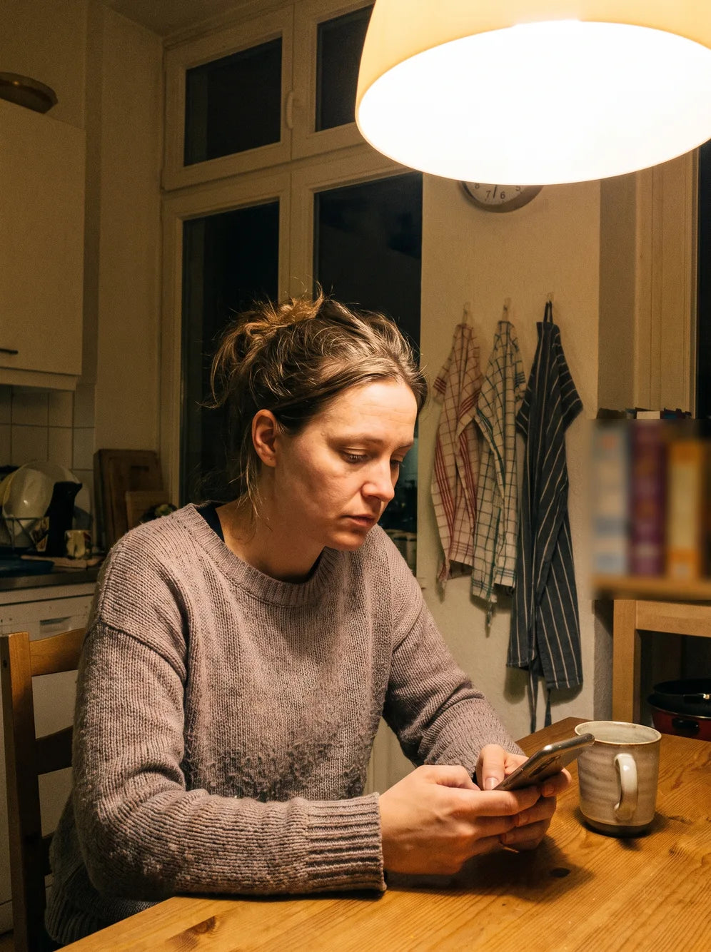 A mother at her kitchen table in the evening, looking at her phone