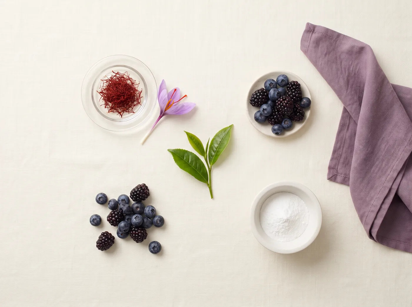 Saffron threads, a crocus flower, green tea leaves and berries on linen
